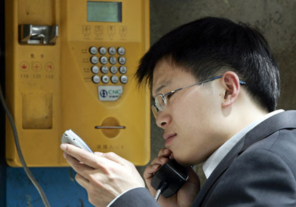 A man chats on a public telephone while checking his mobile phone in Beijing April 24, 2006.