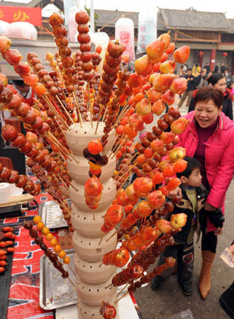 People walk past a bundle of Tanghulu in Nanning, capital of south China's Guangxi Zhuang Autonomous Region, Feb. 10, 2008. Tanghulu is a kind of traditional snack in north China in winter. It is usually made by sugar-coated haws on a stick. Nowadays Tanghulu can be also made by other kinds of fruits and vegetables including yam, apple and orange. The 2nd tourism temple fair of Nanning City opened on an ancient street called Yongzhou on Sunday. About 100,000 people attended the temple fair to taste various kinds of snacks from different places in the nation. 