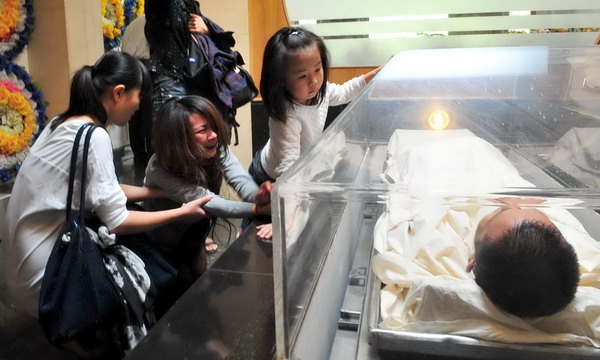 The dead body of Niu Zuotao lies in a coffin on Oct 21 as his wife and daughter bid a final farewell in Guangzhou. Drowned man declared a hero