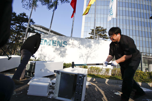 Luo Yonghao (right) uses a hammer to smash Siemens refrigerators, which he and many netizens claim to have design flaws, in front of the company's China headquarters in Beijing on Sunday. Fu Zengkai / for China Daily Blogger smashes 'faulty' Siemens fridge for recall