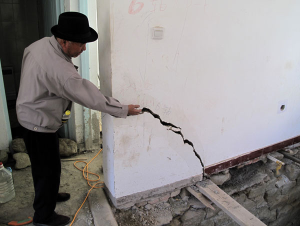Su Jinshi, a 60-year-old villager in Wulapo, Urumqi, examines a crack in his house on Wednesday. Mao Weihua / China Daily Faulty houses found in Urumqi's settlement