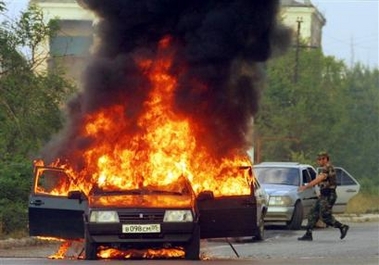 An armed man runs toward a burning car, set ablaze by unidentified gunmen who opened fire on the car in the Chechen capital Grozny, Tuesday, Aug. 9, 2005.