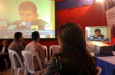 Syrians in Damascus watch as Husam Taher Husam, a Syrian, who is better known as the 'hooded witness' in the U.N. probe into the assassination of former Lebanese Prime Minister Rafiq Hariri, speaks during a press conference broadcast live on Syrian TV.