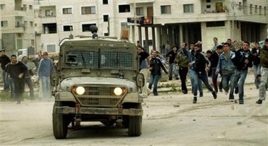 Palestinians hurl stones at an Israeli army vehicle during an Israeli incursion searching for militants in the West Bank town of Jenin Wednesday Dec. 21, 2005.