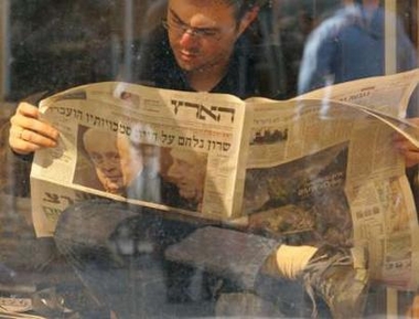 man reads a Hebrew newspaper displaying a photo of ailing Israeli Prime Minister Ariel Sharon at a bus stop in front of the emergency ward of the Haddasah Enkerem hospital in Jerusalem January 7, 2006.