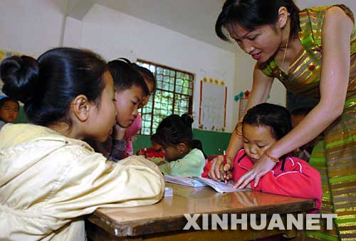 2004年12月3日，云南省西雙版納傣族自治州景洪市勐罕鎮曼聽村的黨員、教師玉罕約（右一）在給村小學的孩子們補習功課。曼聽村是一個典型的傣族村寨，近兩年來，曼聽村黨支部大力加強基層黨組織建設，村黨支部充分發揮黨員在經濟建設中的作用，帶領群眾學科技、調結構、闖市場，開辦科技講座和黨課培訓，使得村里經濟發展迅速，人民生活明顯改善。 新華社發 