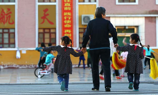 An elderly woman leads her twin granddaughters across the street. Many workers in the space center enlist their parents' help in taking care of the young children. Home of space dreams