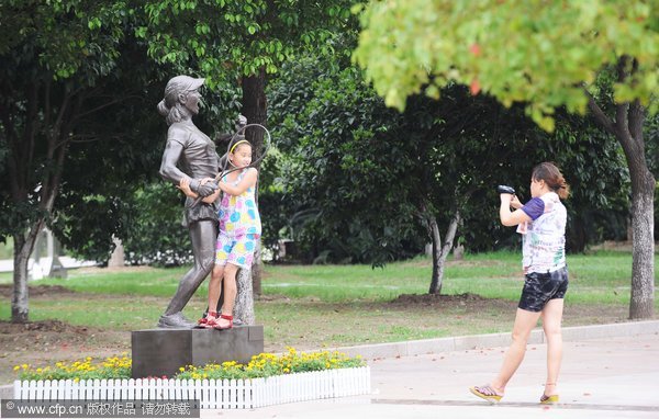 A girl poses for a photo beside a statue of Chinese tennis great Li Na at a square in Wuhan, July 12, 2011. Tennis great immortalized with statue in Wuhan