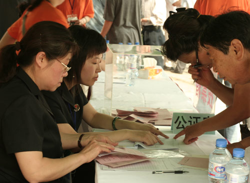 Two notary officials check the documents of voters at the venue for a vote on demolishment and reconstruction of old buildings in Juixiaqiao Sub-district in Beijing, June 9, 2007. Local government and the real estate developer jointly organize the vote on Saturday to see if majority residents of over 5000 families accept the new compensation policy after failed attempts to reach an agreement through other ways. Both notary officials and supervisors are invited to monitor the vote that runs from 9 a.m. to 9 p.m. at six ballot booths. [Sun Yuqing/www.szjzcy.com]