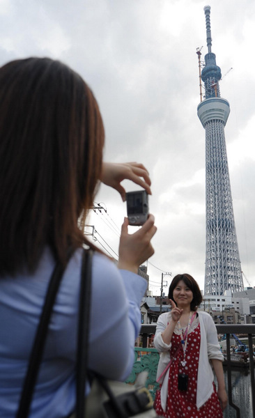 A woman poses for photo in front of the under-construction 'Tokyo Sky Tree' tower in Sumida, Tokyo, Japan, June 8, 2011. Tokyo Sky Tree: world's highest self-standing tower