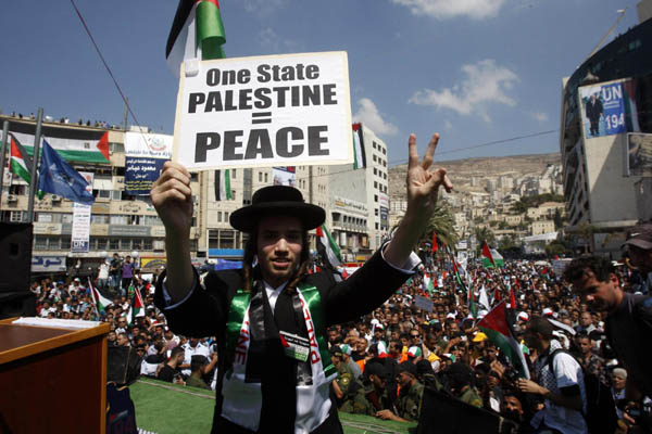 A member of Neturei Karta, a fringe Jewish Ultra-Orthodox movement within the anti-Zionist bloc, holds a placard as he stands on a stage during a rally in the West Bank city of Nablus September 21, 2011. Palestinians rally for the UN statehood bid