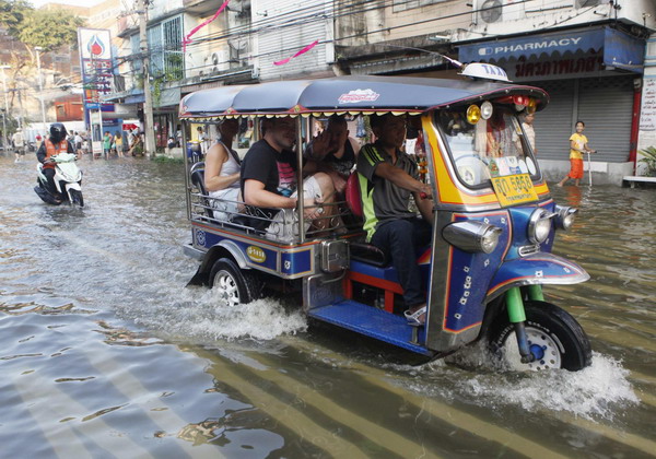 Tourists sits on a tricycle taxi called a 'tuk-tuk' as they travel along a flooded street at Phranakhon district in Bangkok October 24, 2011. Bangkok on high alert with worst floods in 50-yrs