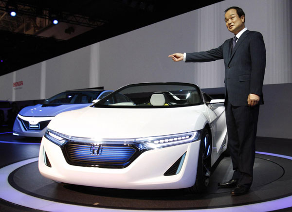 Honda Motor Co President Takanobu Ito poses next to the company's next-generation EV sports car EV-Ster (C) and next-generation plug-in hybrid vehicle AC-X during a news conference at the 42nd Tokyo Motor Show in Tokyo November 30, 2011. Tokyo Motor Show kicks off