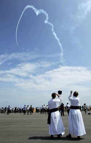 Two chaplains from Canada and Belgium watch a performance of the Rebel 300 aerobatic aircraft flown by Tony Blair of Australia's Blair Aerosports during an aerial display at the Singapore Airshow in Singapore February 16, 2012. Singapore holds largest airshow in Aisa