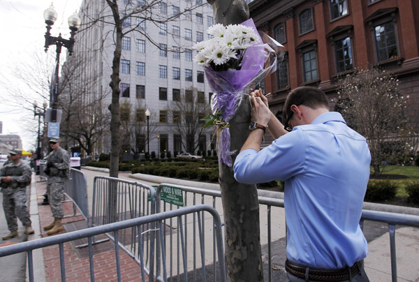 A man ties a bouquet of flowers onto a tree at the edge of a barricade set up along Boylston Street a day after two explosions near the finish line of the Boston Marathon, Massachusetts April 16, 2013. Boston mourns bombing victims