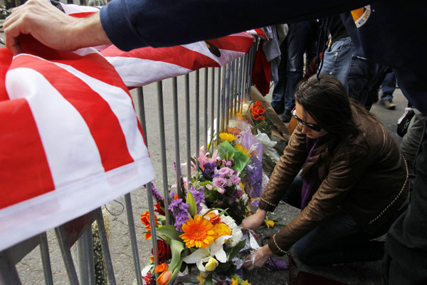 A woman places flowers at a makeshift memorial at a barricaded entrance to Boylston Street a day after two explosions near the finish line of the Boston Marathon, Massachusetts April 16, 2013. Boston mourns bombing victims