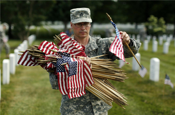 A soldier from the Third US Infantry Regiment (The Old Guard) carries flags to be placed beside graves at Arlington National Cemetery in Virginia, May 23, 2013. Remembrance before Memorial Day