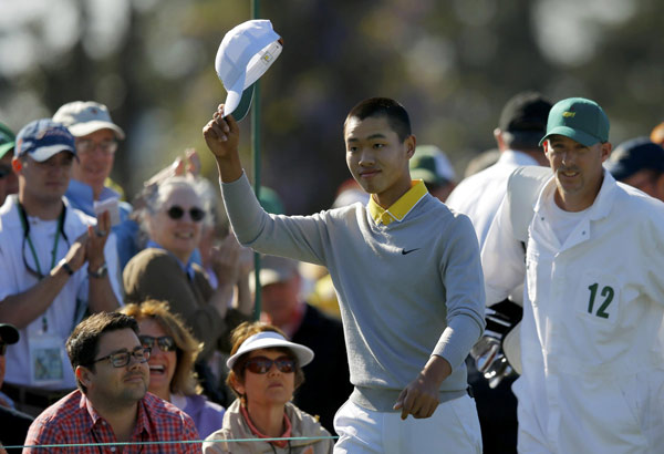 Amateur Guan Tianlang of China tips his hat to the crowd as he walks onto the first tee with caddie Brian Tam (R) during third round play in the 2013 Masters golf tournament at the Augusta National Golf Club in Augusta, Georgia, April 13, 2013. Chinese teen golfer draws young admirers