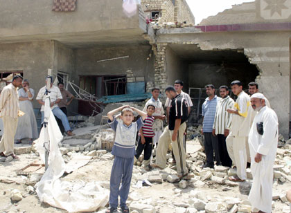 Iraqis stand outside a house damaged by a rocket attack in Baghdad May 6, 2006. Two children ages 5 and 6 were killed and three adult civilians were wounded when a mortar round landed on Baghdad's western district of Shula on Saturday, police said.