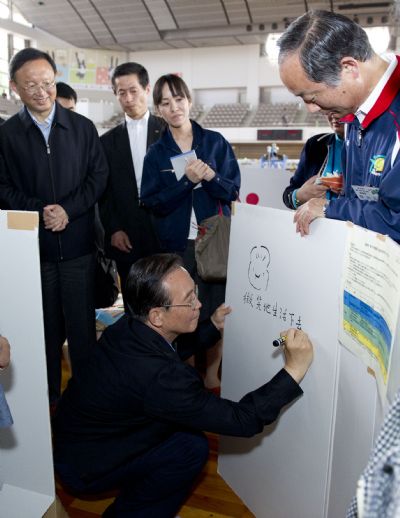 Chinese Premier Wen Jiabao draws a smiling face and writes down his good wishes to disaster victims on a white board, encouraging them to smile and live on, at a gymnasium serving as a makeshift shelter in Fukushima, Japan, May 21, 2011. Fukushima was ravaged by a powerful earthquake and devastating tsunami on March 11. Premier Wen visits disaster-ravaged Fukushima