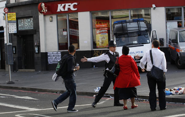 A police officer keeps pedestrians from crossing into a crime scene after overnight looting in Brixton, south London August 8, 2011. UK police arrest over 160 in weekend London riots