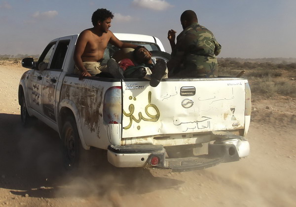 Anti-Gaddafi fighters with an injured comrade travel in a vehicle during heavy shelling by Gaddafi loyalists near Herawa, 52 km (32 miles) east of Sirte, Sept 18, 2011. Libya's NTC vows to capture Gadhafi hometown soon