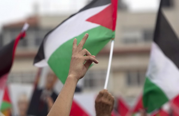A Palestinian gestures in front of a flag during a rally in the West Bank city of Ramallah upon President Mahmoud Abbas' return from the UN General Assembly in the US, Sept 25, 2011. Abbas: No talks without Israeli settlement freeze