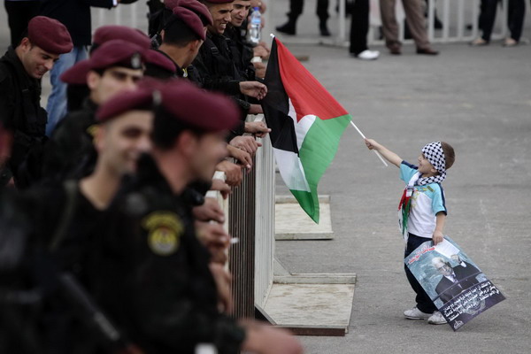 A Palestinian boy holds a flag in front of members of the Palestinian security forces in the West Bank city of Ramallah, before a celebration upon President Mahmoud Abbas' return from the United States Sept 25, 2011. Abbas: No talks without Israeli settlement freeze